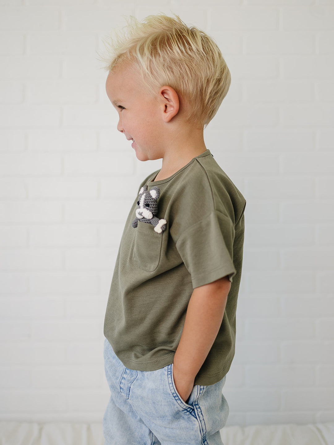Child wearing an olive green t-shirt with a crochet frenchie design on a plain background